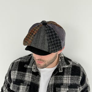 May include: A multi-patterned newsboy cap with a black brim. The cap features sections of brown, gray, and black fabrics in herringbone, houndstooth, and other patterns. The person is wearing a black and white plaid shirt.