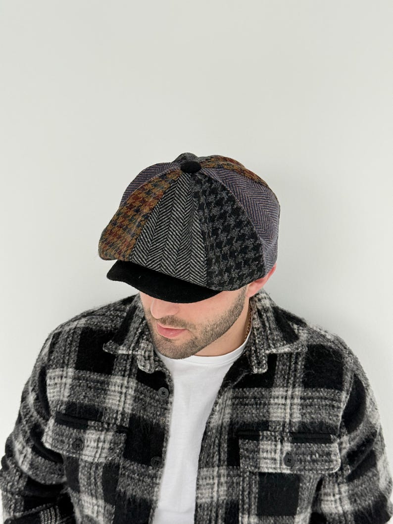 May include: A multi-patterned newsboy cap with a black brim. The cap features sections of brown, gray, and black fabrics in herringbone, houndstooth, and other patterns. The person is wearing a black and white plaid shirt.