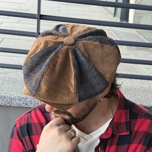 Puede incluir: Una gorra de estilo boina de ocho paneles confeccionada con paneles alternos de pana marrón lisa y tela con estampado de pata de gallo en azul y marrón. La gorra presenta un botón central forrado en la parte superior y una visera corta.