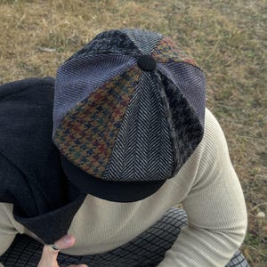 May include: A patchwork newsboy cap with a black brim and a button on top. The cap features panels of various patterned fabrics, including herringbone and tweed, in shades of gray, brown, and blue.