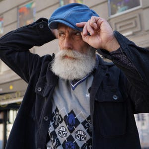 May include: A man wearing a blue denim cap, a black corduroy jacket, and a gray sweater with a black and blue geometric pattern featuring Star Wars characters.