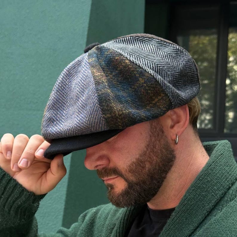 May include: A multi-toned newsboy cap with a black brim. The cap features a patchwork design with gray, blue, and brown herringbone and plaid patterns. The cap is made of a textured fabric.