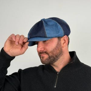 May include: A two-tone denim newsboy cap in shades of blue. The cap has a rounded crown and a short, stiff brim. The cap is made of denim fabric and has visible stitching. The cap is a classic style, suitable for casual wear.