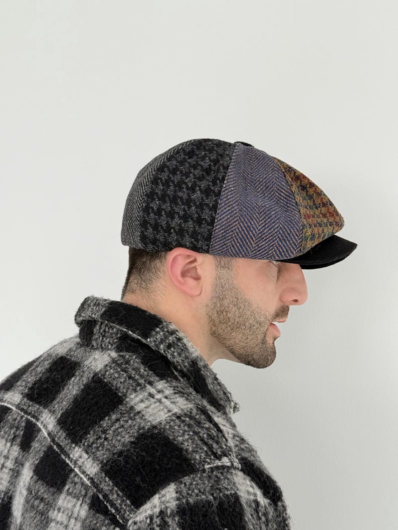 May include: A patchwork newsboy cap featuring panels of gray houndstooth, herringbone, and tweed patterns. The cap has a black brim and is worn by a person wearing a black and white plaid shirt.