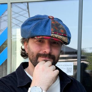 May include: A newsboy cap constructed from blue denim fabric, featuring a multi-paneled design with a decorative woven textile insert in shades of red, black, and tan. The cap has a rounded crown, a central button, and a short, stiffened brim.