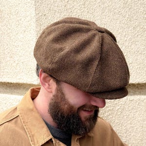 Peut inclure: Une casquette gavroche marron avec un motif à chevrons classique. La casquette est composée d'une calotte à plusieurs panneaux et d'une visière courte et rigide. Le tissu présente un tissage texturé avec des variations de tons marron.