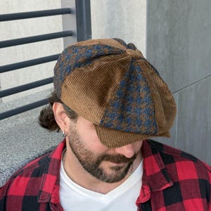 May include: An eight-panel newsboy cap featuring alternating sections of solid brown corduroy fabric and blue and brown houndstooth patterned fabric. The cap has a structured brim and a central button detail at the top of the crown.