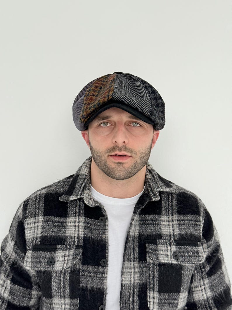 May include: A patchwork newsboy cap with a black brim. The cap features panels of brown, gray, and black patterned fabric. The person in the image is wearing a black and white plaid shirt and a white t-shirt.