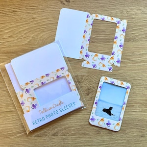 Peut inclure: Un ensemble de trois pochettes photo blanches avec un motif de biberon et de sucette. Les pochettes sont conçues pour contenir une photo de taille standard. Le texte "NelliumCrafts RETRO PHOTO SLEEVES" est imprimé sur le devant des pochettes.