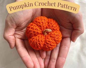 Może przedstawiać: Ręcznie robiony pomarańczowy dyni z brązowym trzonkiem. Dynia jest trzymana w dłoniach. Tekst "Pumpkin Crochet Pattern" znajduje się nad dynią.