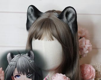 May include: A pair of black and gray faux fur wolf ears attached to a wig with light brown hair. The ears are detailed with a realistic texture and shape. The wig is styled on a mannequin head, with pink flowers in the background.