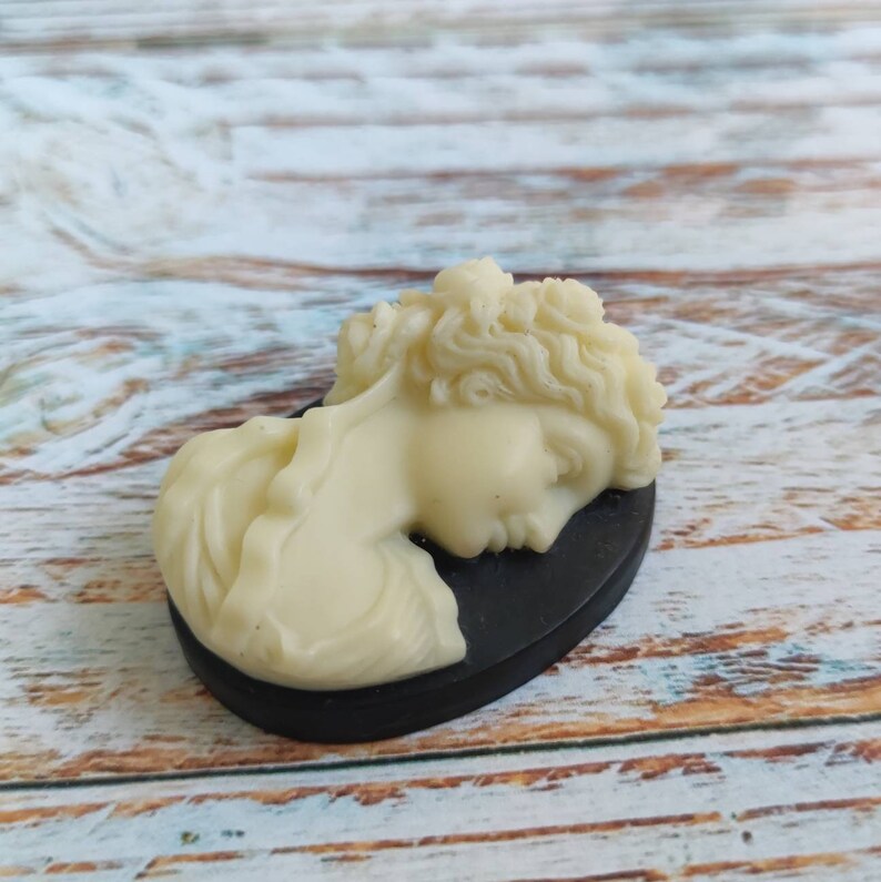 May include: A white cameo featuring a woman's profile with detailed hair and a black oval background.