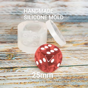 May include: A clear silicone mold for crafting dice, with a red die showing white dots and a triangle. The text "HANDMADE SILICONE MOLD" and "25mm" are visible. The die measures approximately 1 inch.