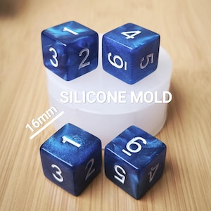 Op de afbeelding: Vier blauwe harsdobbelstenen met witte cijfers, elk 16 mm groot, liggen op een witte siliconen mal. De dobbelstenen hebben een gemarmerd effect. De tekst "SILICONE MOLD" is zichtbaar op de mal.