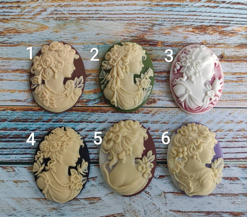 May include: Six cameo pendants with different designs featuring women's profiles. The cameos are in various colors, including brown, green, white, and purple.