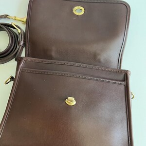 May include: Open, brown leather shoulder bag with a flap closure and gold-tone hardware. The bag has a long, adjustable strap and a spacious interior. The bag's design is classic and timeless, suitable for everyday use.
