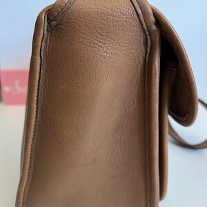 May include: A brown leather shoulder bag with a flap closure and a gold-toned buckle. The bag has a smooth, textured surface and a slightly rounded shape.