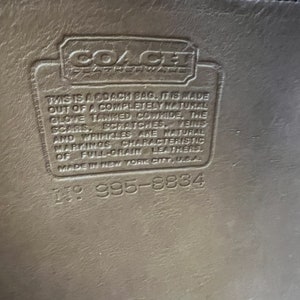 May include: Close-up of a brown leather Coach bag tag with the text "This is a Coach bag. It is made out of a completely natural glove tanned cowhide. The scars, scratches, veins and wrinkles are natural markings characteristic of full-grain leathers. Made in New York City, USA." and the number "1995-8834".