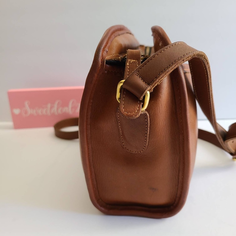 May include: A brown leather crossbody bag with a gold buckle and a long adjustable strap.