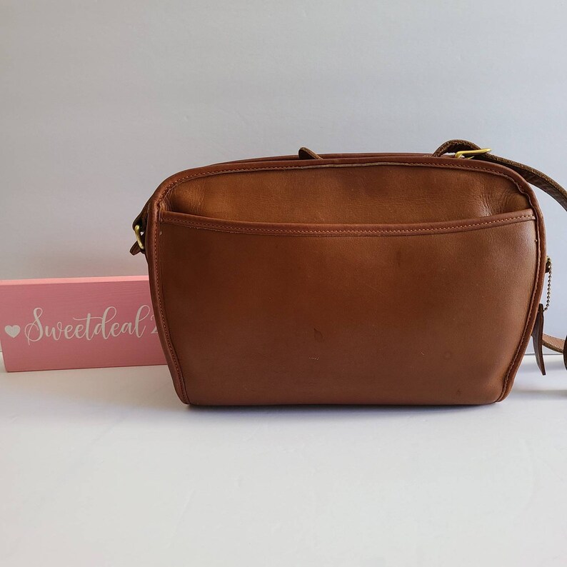 May include: A brown leather shoulder bag with a gold buckle and zipper. The bag has a flap closure and a single strap.