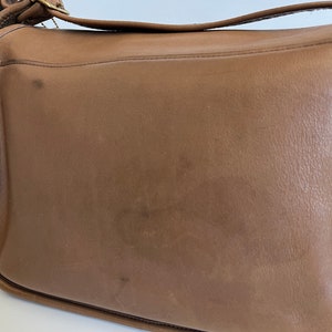 May include: A brown leather shoulder bag with a gold buckle and strap.