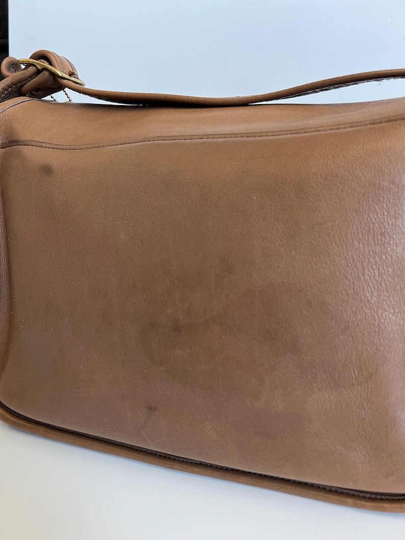May include: A brown leather shoulder bag with a gold buckle and strap.