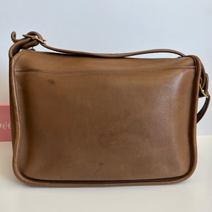 May include: A brown leather shoulder bag with a flap closure and a gold buckle. The bag has a single strap and is made of a soft, supple leather.