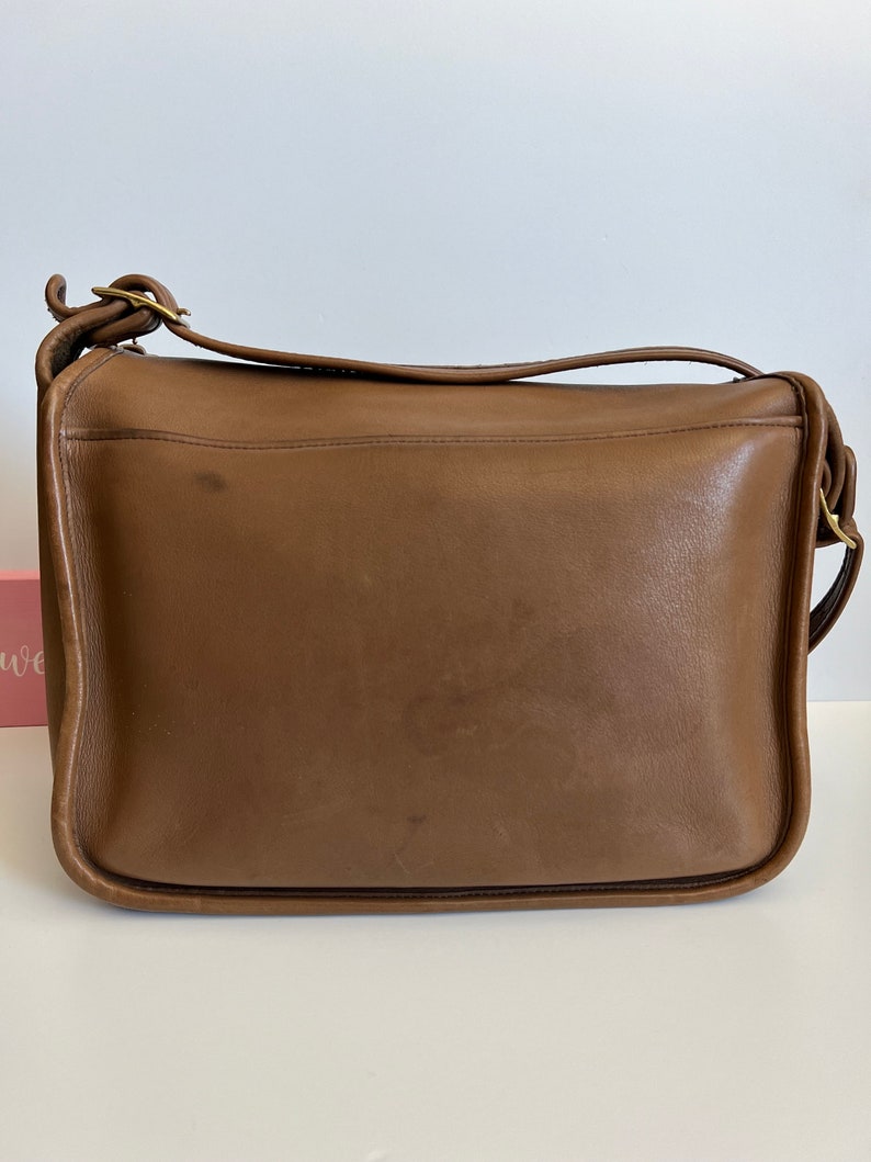 May include: A brown leather shoulder bag with a flap closure and a gold buckle. The bag has a single strap and is made of a soft, supple leather.