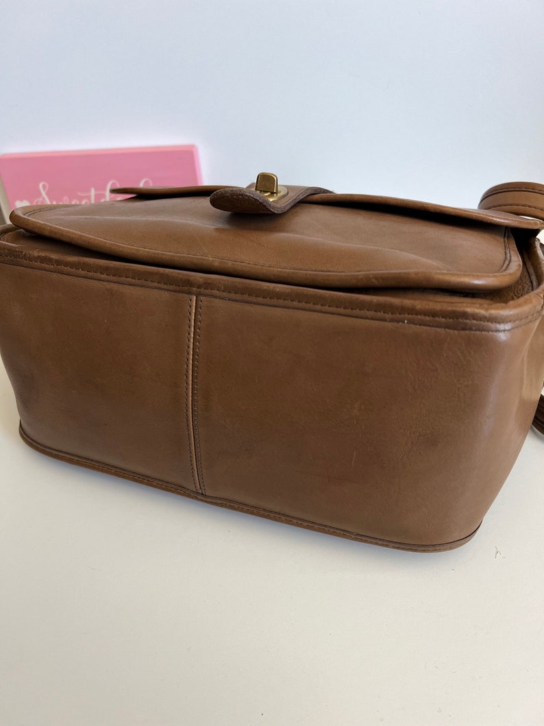 May include: A brown leather shoulder bag with a brass clasp. The bag has a rectangular shape and a flap closure.
