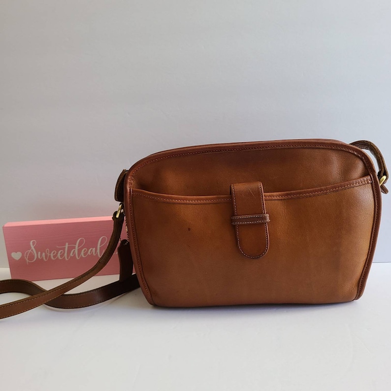 May include: A brown leather shoulder bag with a flap closure and a gold-toned buckle. The bag has a single strap and a small pocket on the front.