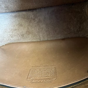 May include: Close-up of the inside of a brown leather purse with a zipper closure. The purse has a Coach label with the text "Coach 588-9284" and a small leather tag with the number "40705".