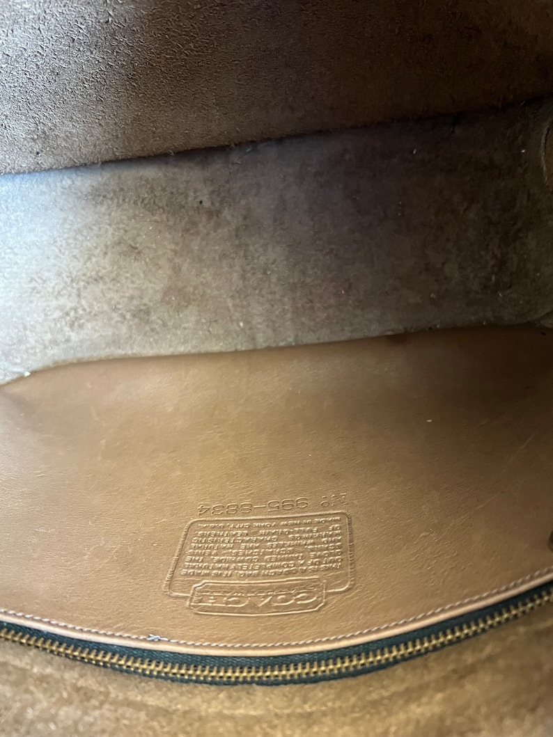 May include: Close-up of the inside of a brown leather purse with a zipper closure. The purse has a Coach label with the text "Coach 588-9284" and a small leather tag with the number "40705".