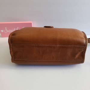 May include: A brown leather handbag with a single buckle closure. The bag is shown from the bottom, with the stitching visible.