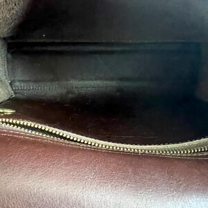 May include: Interior view of a brown leather handbag. The inside is dark with a zipper at the bottom. The leather has a smooth texture. The bag appears to be empty.