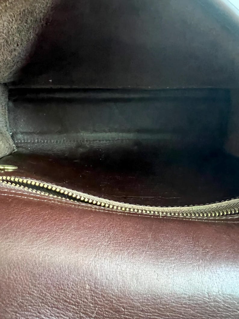 May include: Interior view of a brown leather handbag. The inside is dark with a zipper at the bottom. The leather has a smooth texture. The bag appears to be empty.