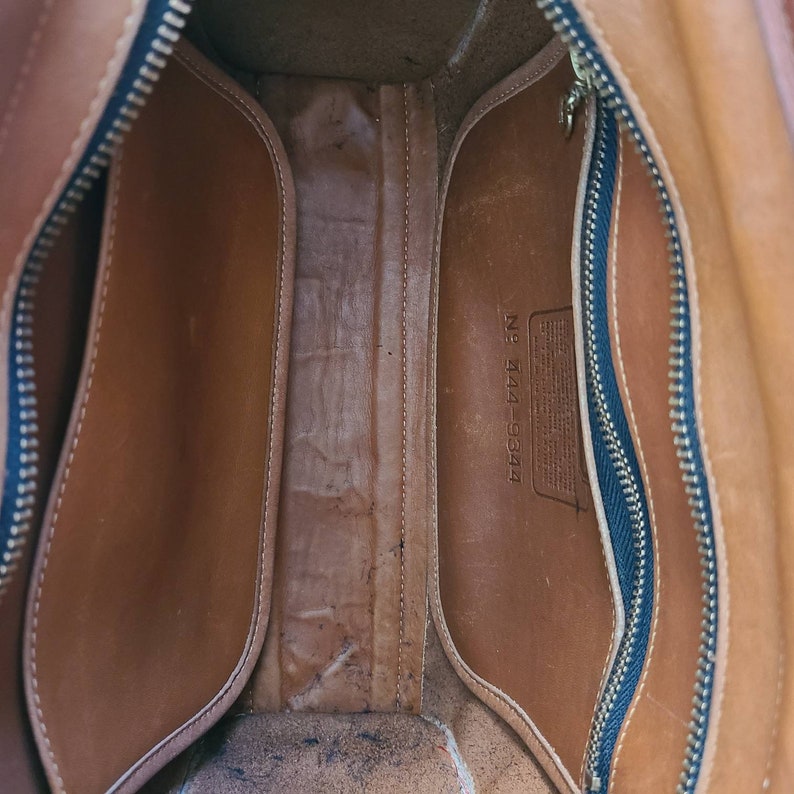 May include: The inside of a brown leather bag with a zipper closure. The bag has a label that reads "No. 144-9344".
