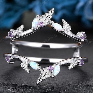 May include: A silver ring guard with a leaf design, featuring white and purple gemstones. The ring guard is designed to sit around another ring. The background is a dark surface with blue flowers.