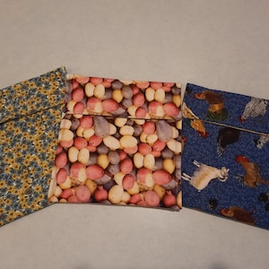 May include: Three square fabric pouches with fold-over flaps. The left pouch features a blue and yellow sunflower pattern. The center pouch displays a print of assorted red, yellow, and purple potatoes. The right pouch shows a blue background with chickens.