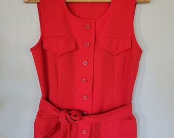 May include: A sleeveless, red vest with a matching belt and button-up front. The vest has two front pockets and the text "ACT III" on the label. The garment is hanging on a wooden hanger.