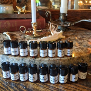May include: A collection of small brown glass bottles with black caps and white labels. The labels have various text on them, including "Scorch", "Shine", "Law Be Just", "Blaze My Way", "Sweet Heartship", "Eye of the Waters", "Slipped the Net", "Arm", and "Tide Change".