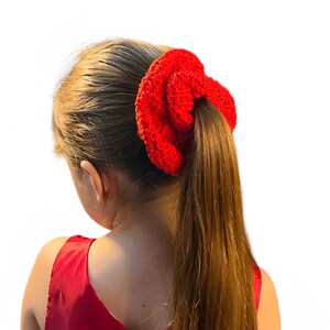 May include: A red crocheted hair scrunchie with a textured surface. The scrunchie is tied around a ponytail.