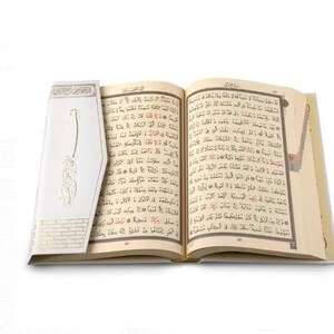 May include: An open book with white pages and gold accents. The book is open to a page with Arabic text. The book is on a white background.
