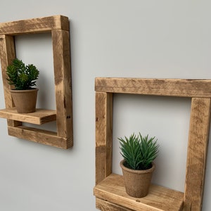 May include: Two rustic wooden shelves with a square frame and a small shelf. Each shelf has a potted succulent plant on it.