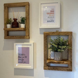 May include: Three rustic wooden shelves with a white frame, each with a potted plant and a framed print. The prints feature inspirational quotes: "Do the things that make you happy", "Whit's fur ye'll no go past ye."