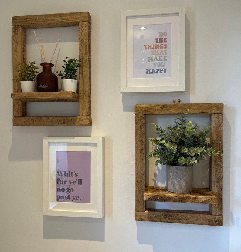 May include: Three rustic wooden shelves with a white frame, each with a potted plant and a framed print. The prints feature inspirational quotes: "Do the things that make you happy", "Whit's fur ye'll no go past ye."