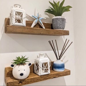 May include: Two rustic wooden shelves with decorative items. The top shelf has a white lantern, a blue and white starfish, and a potted green plant. The bottom shelf has a white lantern, a blue and white ceramic diffuser, and a white ceramic planter with a bear face.