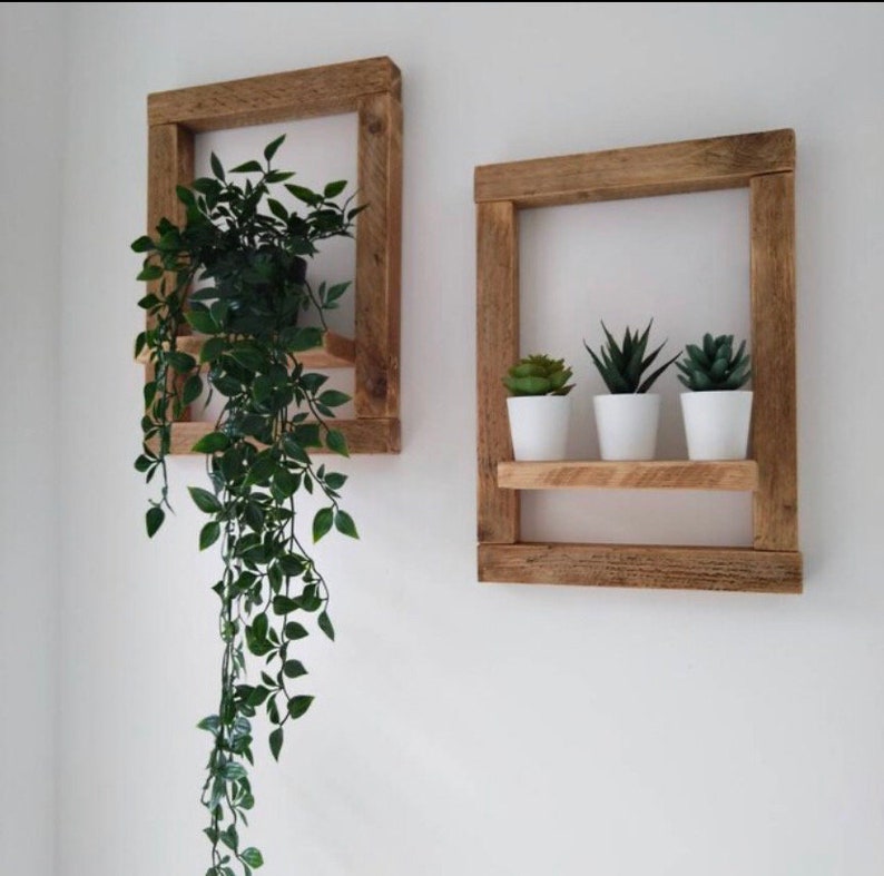 May include: Two rustic wooden wall shelves with a natural wood finish. The top shelf is empty, while the bottom shelf holds three small potted succulents. The shelf on the left has a hanging plant with green leaves.