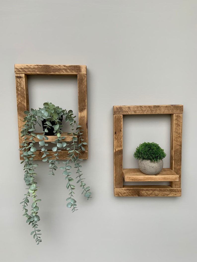 May include: Two rustic wooden shelves with a plant on each. The shelves are made of reclaimed wood and have a natural finish. The plant on the left is a leafy green plant, and the plant on the right is a small green bush.