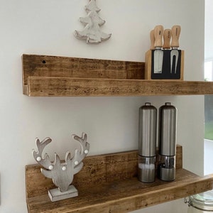 May include: Two rustic wooden shelves with a white wooden reindeer figurine on the bottom shelf and a set of wooden handled kitchen knives in a black holder on the top shelf.