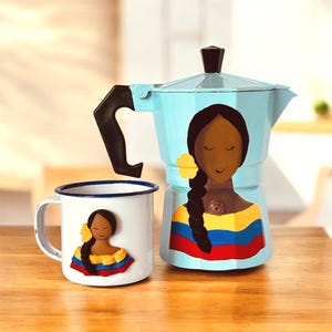 May include: A light blue stovetop espresso maker and a white enamel mug, both featuring a painted design of a woman with dark hair and a yellow flower. The woman is wearing a dress in the colors of the Colombian flag.